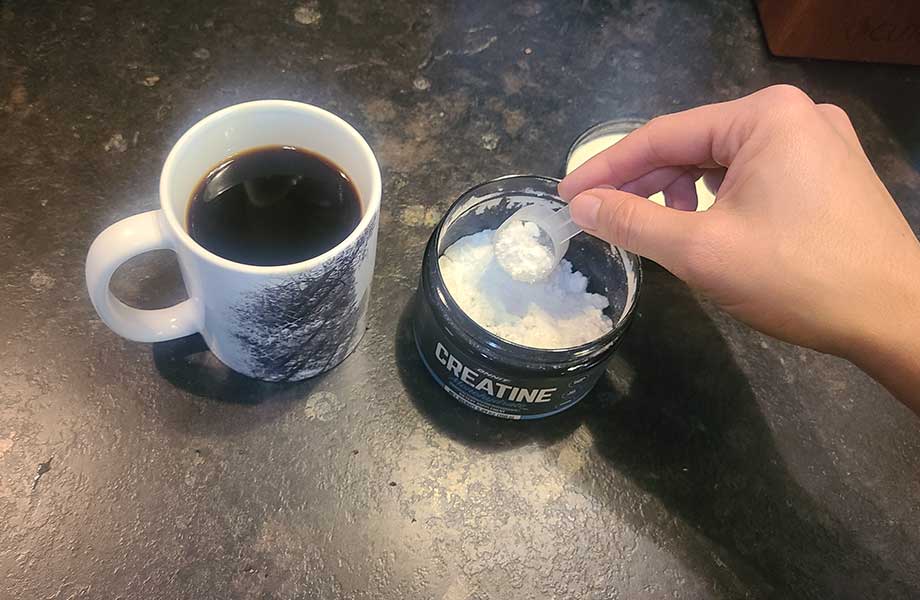 Person scooping creatine into a mug of coffee