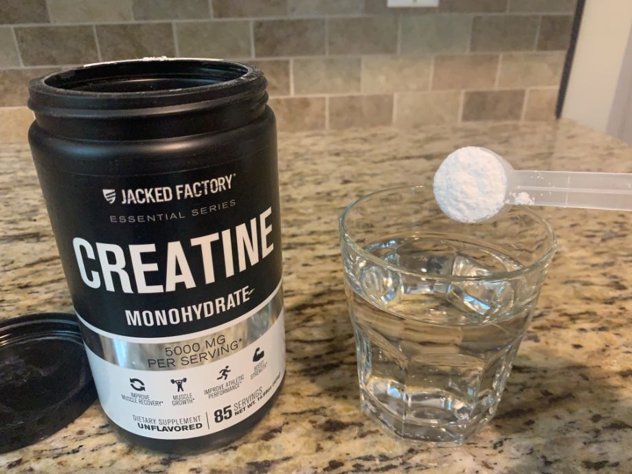 A scoop of Jacked Factory Creatine about to be poured into a glass.