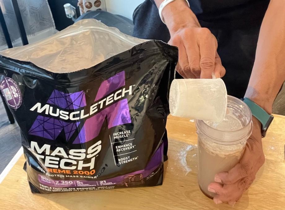 Looking down on a scoop of MuscleTech Mass Gainer as it’s poured into a shaker cup.