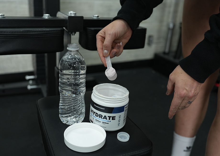 Scooping Transparent Labs Hydrate on a weight bench.