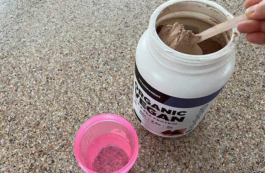 A hand scoops Transparent Labs Vegan Protein powder to dump it into a pink shaker cup