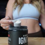 A woman holds up a scoop of XWERKS Ignite Pre-Workout.