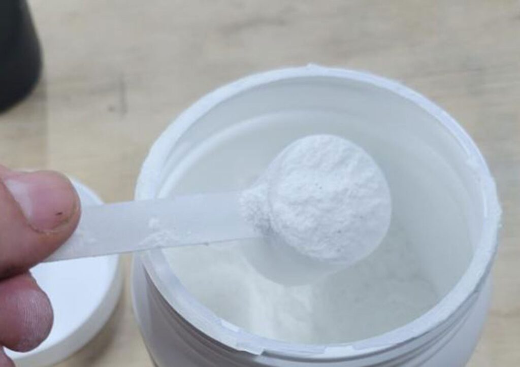 Looking down on a hand as it lifts a scoop of Pre-Workout from the container.