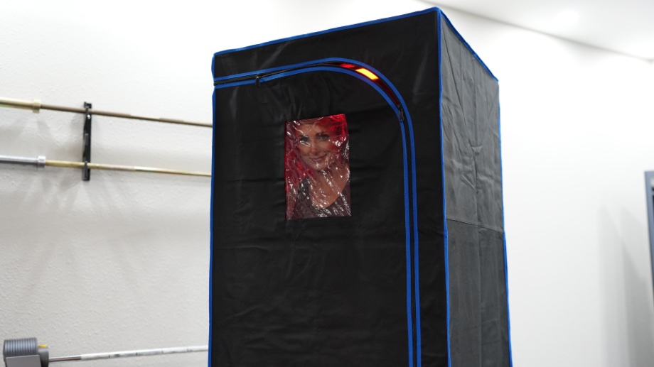 A smiling woman's face can be seen peering out of the window in a SereneLife Full Size Portable Infrared Sauna.