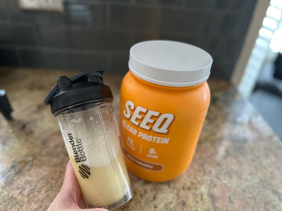 A hand holds a shake made from SEEQ Clear Whey Protein Isolate
