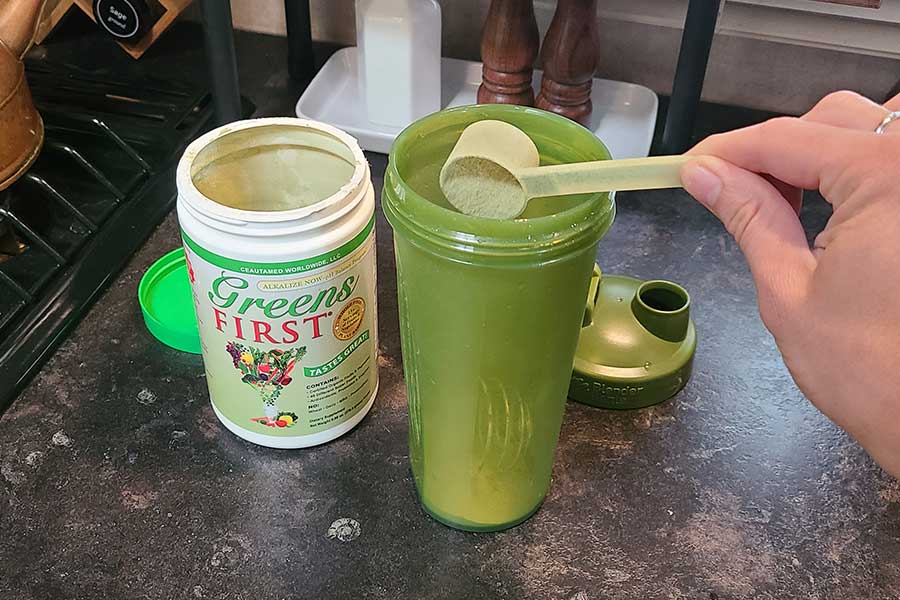 Someon Scooping Greens First Into A Shaker Bottle