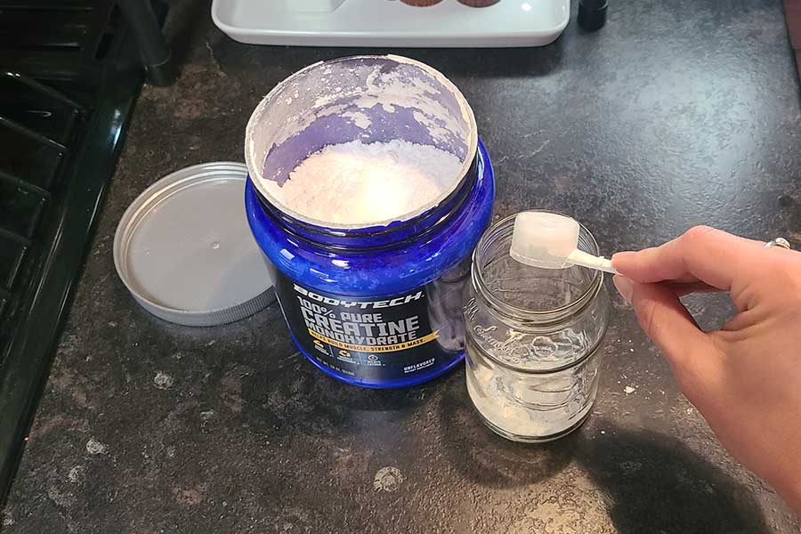 Someone Scooping Bodytech Creatine Into A Glass