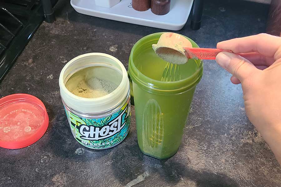 Someone Scooping Ghost Greens Into A Shaker Bottle