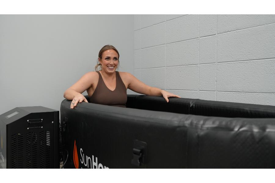 A woman in a brown tank-top sitting in a Sun Home Sauna inflatable cold plunge tub