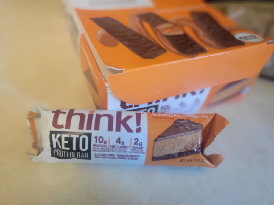 A think! Keto Bar in the wrapper next to a box of bars.