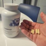 A person holds a few capsules of Thorne Joint Support next to the bottle.