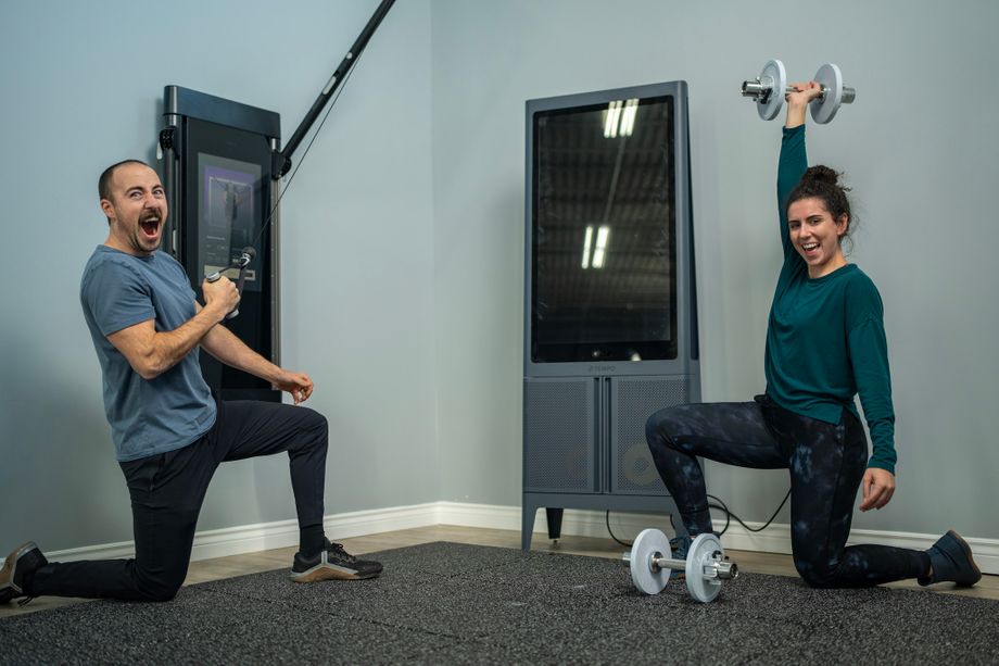 Tonal vs. Tempo: Coop and Amanda exercising with Tonal and Tempo Studio, respectively, in a smart home gym room with blue walls.