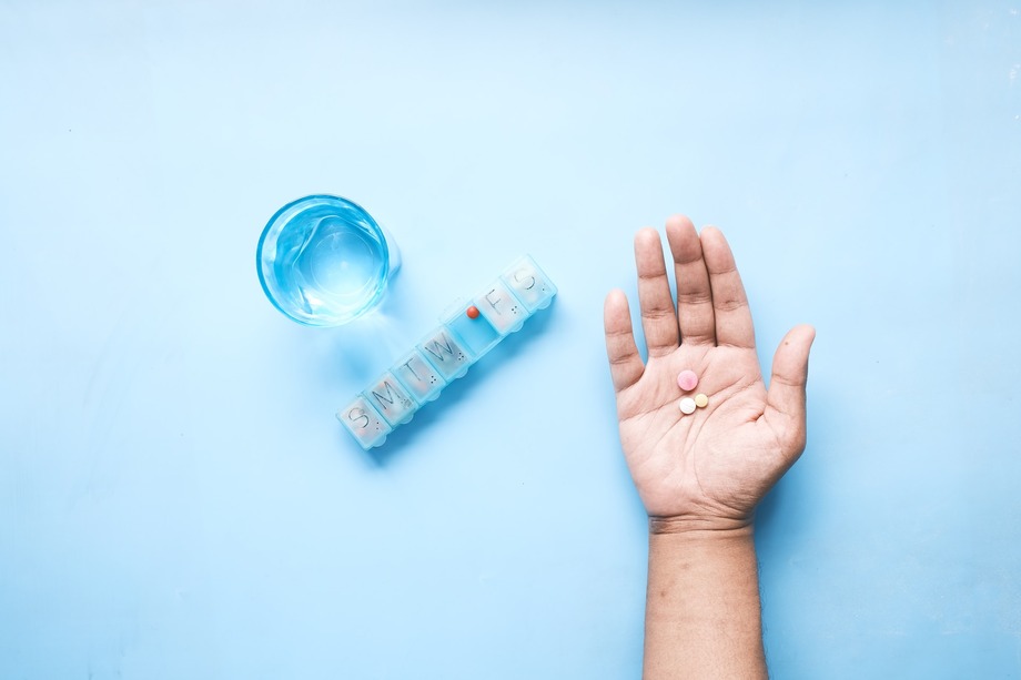 a palm-up hand holding three pills next to a pill organizer