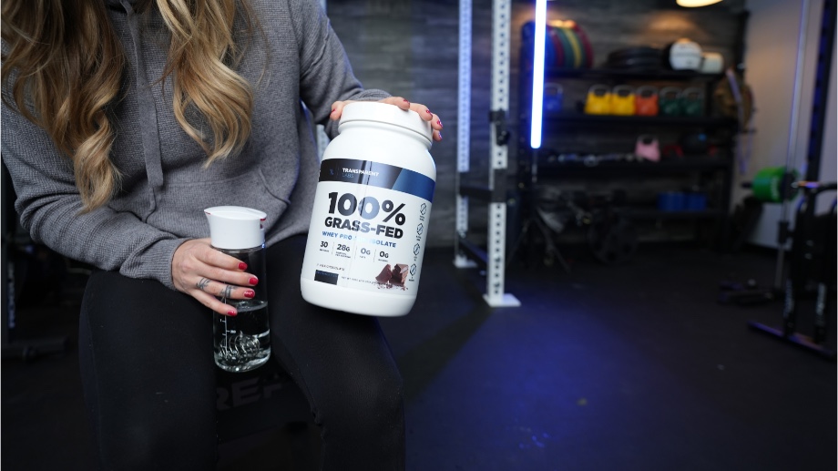 A person holds a container of Transparent Labs 100% Grass-Fed Whey Protein Isolate.