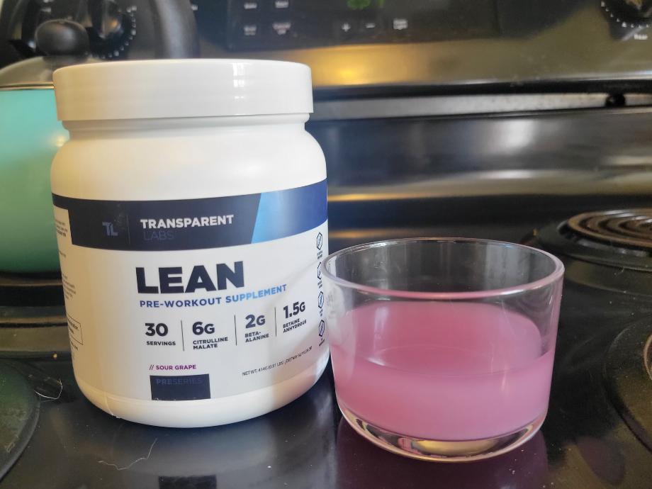 A clear glass containing a pink dose of Transparent Labs Pre-Workout is shown next to the container.