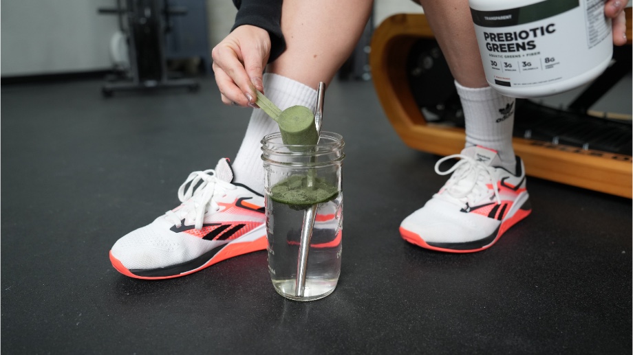 Someone dumping a scoop of Transparent Labs Prebiotic Greens into a glass