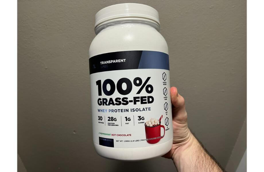 A hand holding Transparent Labs 100% grass-fed whey protein isolate in a sleek white container, emphasizing natural and high-quality protein.