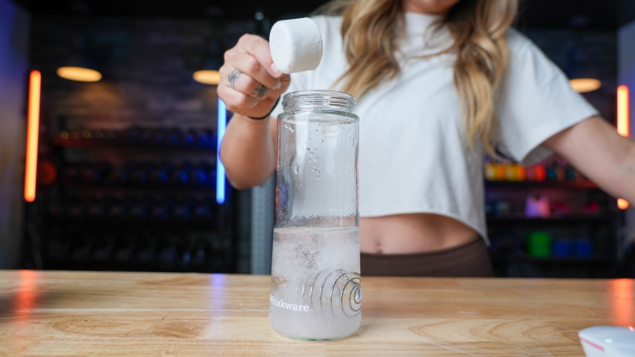 A person is shown pouring a scoop of Transparent Labs Stim-Free Pre-Workout into a shaker glass.