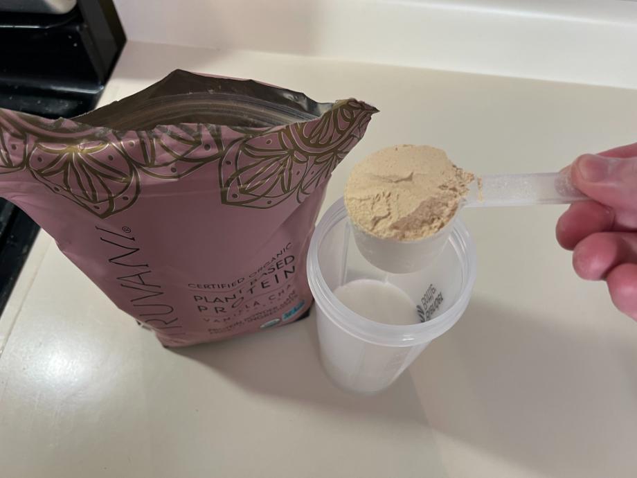 A scoop of Truvani Protein Powder about to be poured into a shaker cup