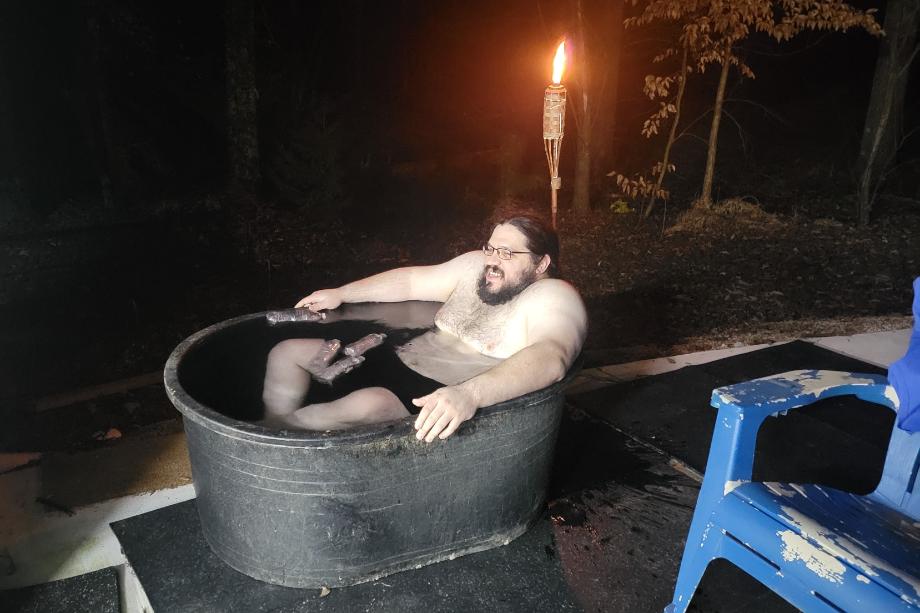 Man chilling in a Tuff Stuff Stock Tank filled with ice water. A tiki torch burns in the background.