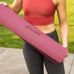 Up close photo of woman holding rolled up maroon Ativafit yoga mat.