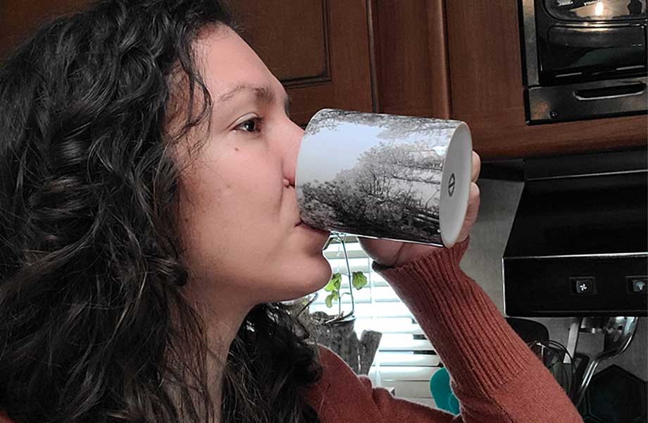 A woman is shown drinking coffee from a ceramic mug.
