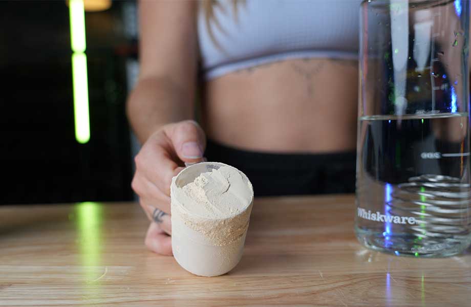 A woman is shown holding up a scoop of Legion Plant+ Protein Powder