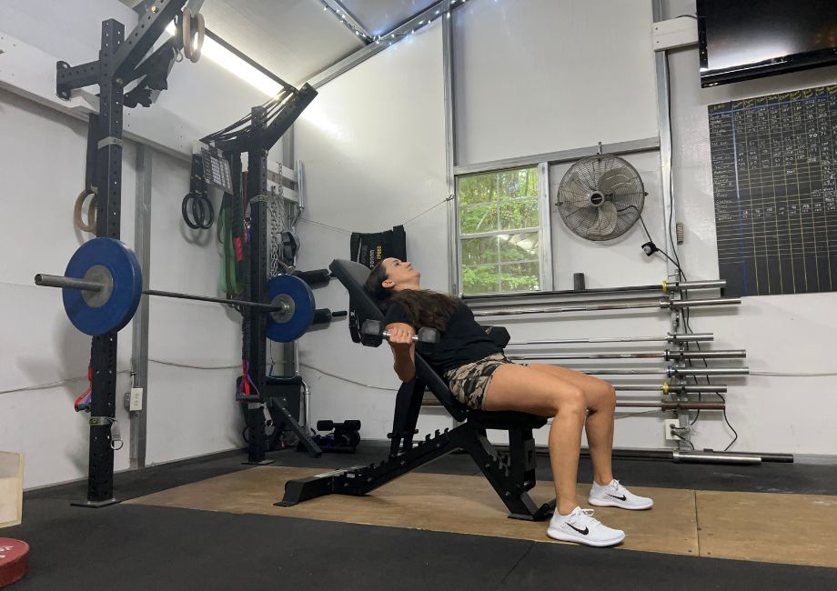 A woman lifting weights on the Force USA Pro Series FID Bench while it's set at an incline