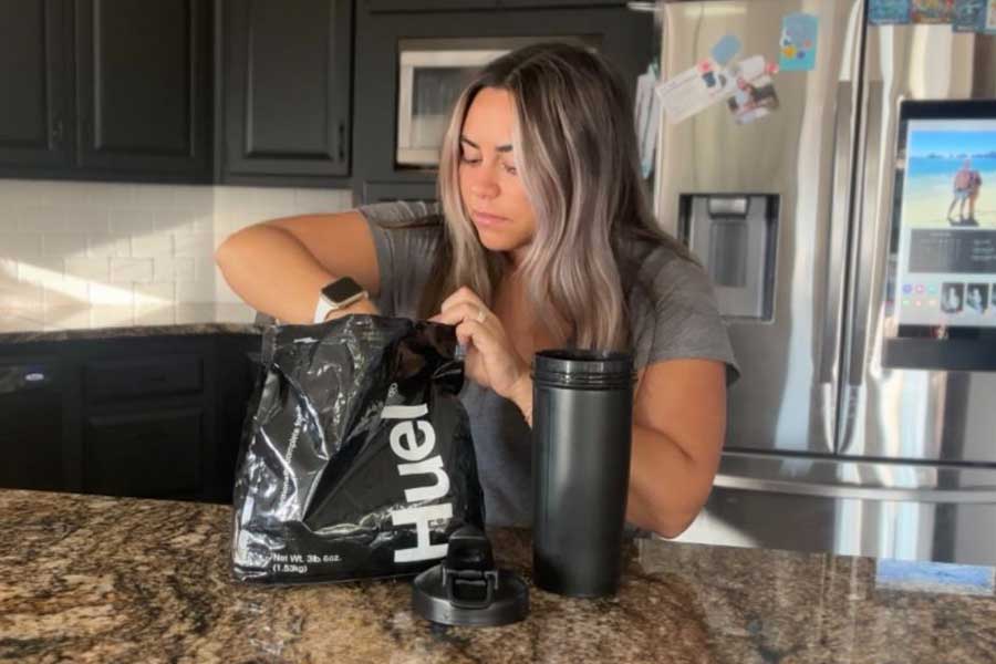 Woman scooping Huel Black out of bag into a shaker bottle