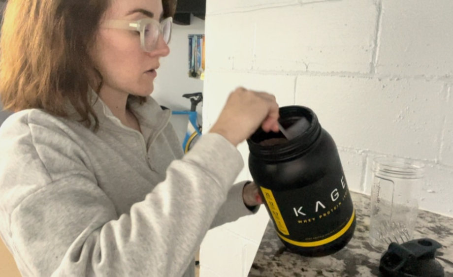A woman scoops Kaged Whey Protein Isolate out of the container.