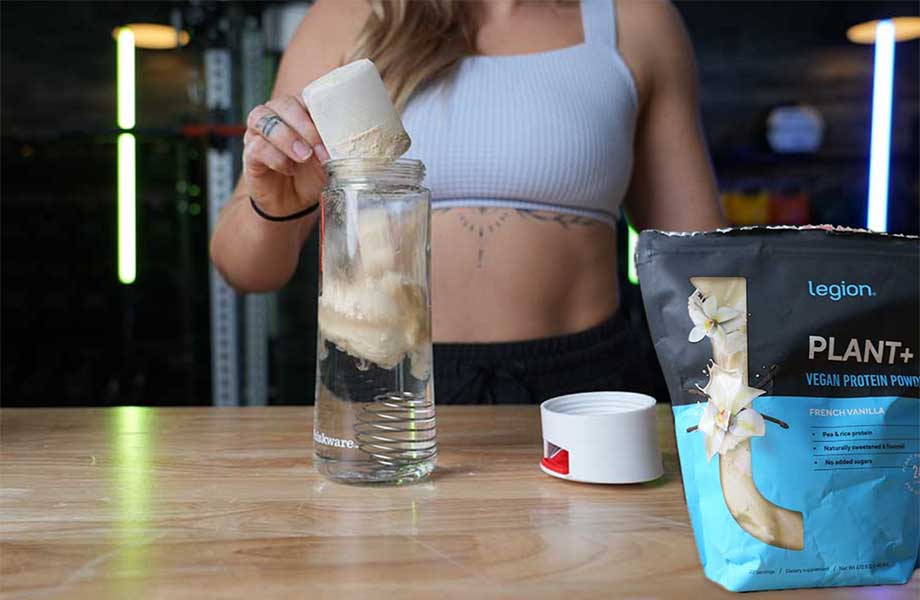 Woman scooping Legion Plant+ Protein into a shaker with the bag on the table