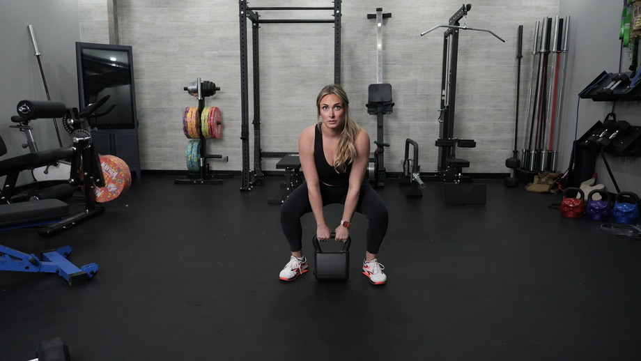 A woman is shown squatting with the PowerBlock Adjustable Kettlebell.