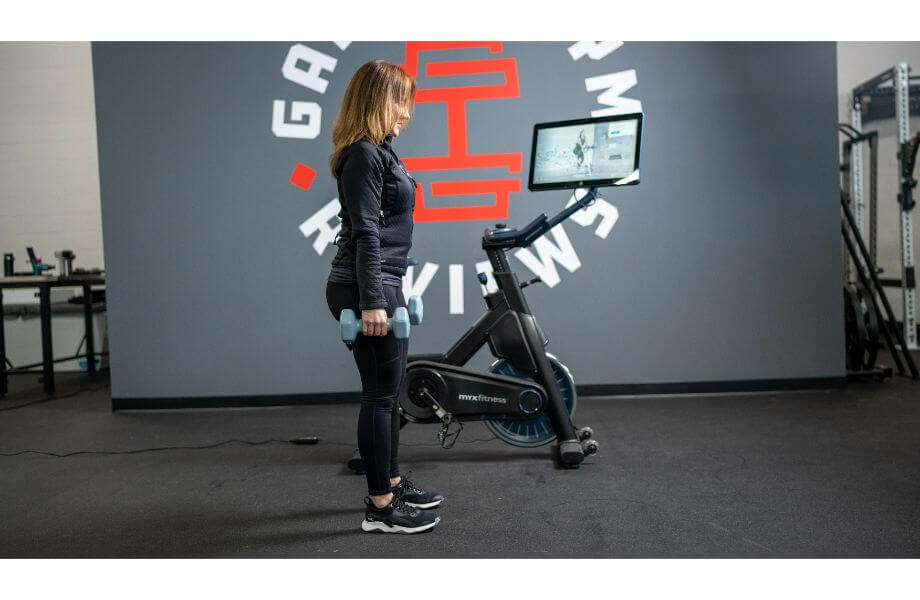 woman standing with weights next to myx II bike